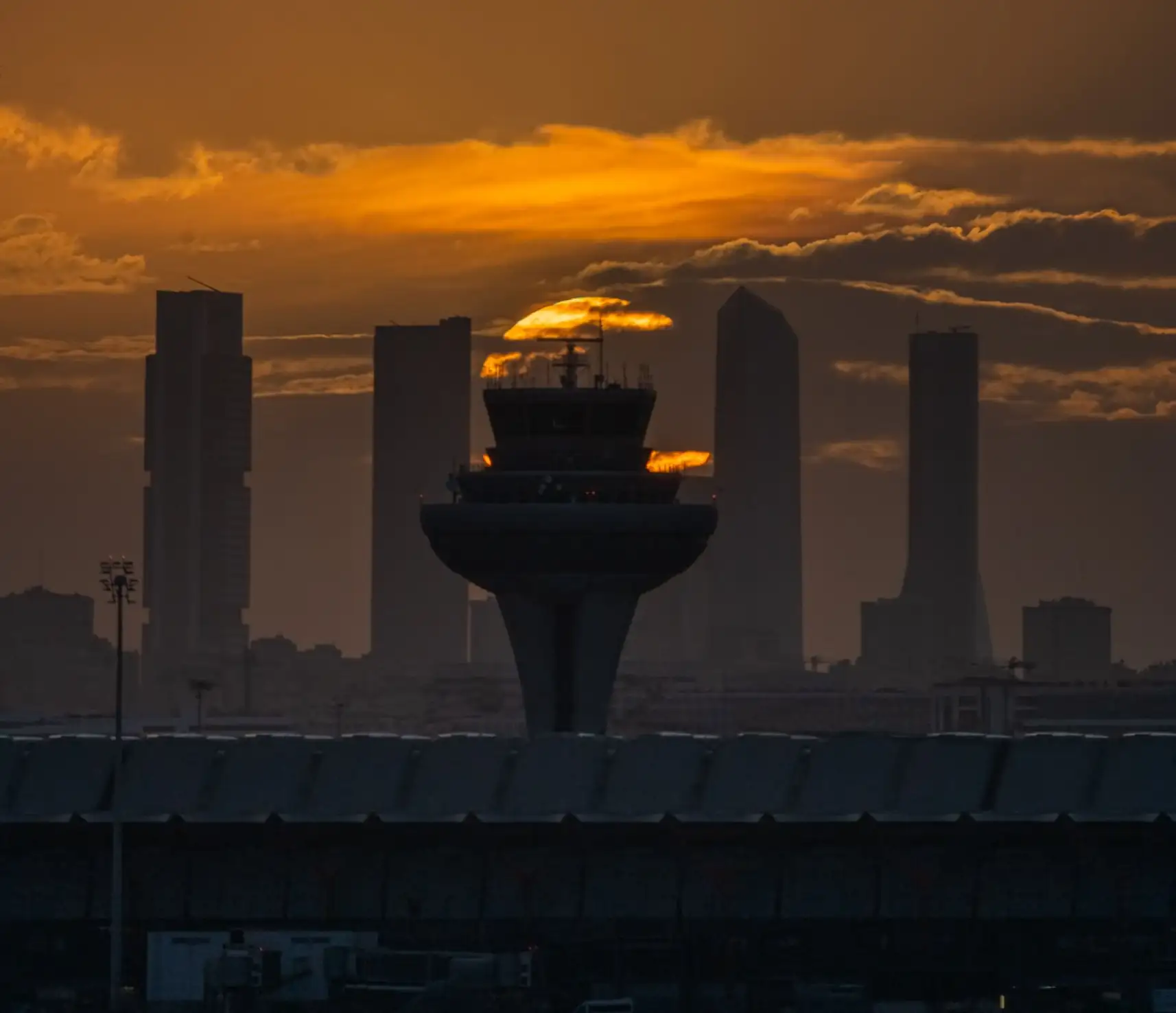 La torre de control del aeropuerto de Madrid-Barajas al atardecer, con los rascacielos de Madrid al fondo